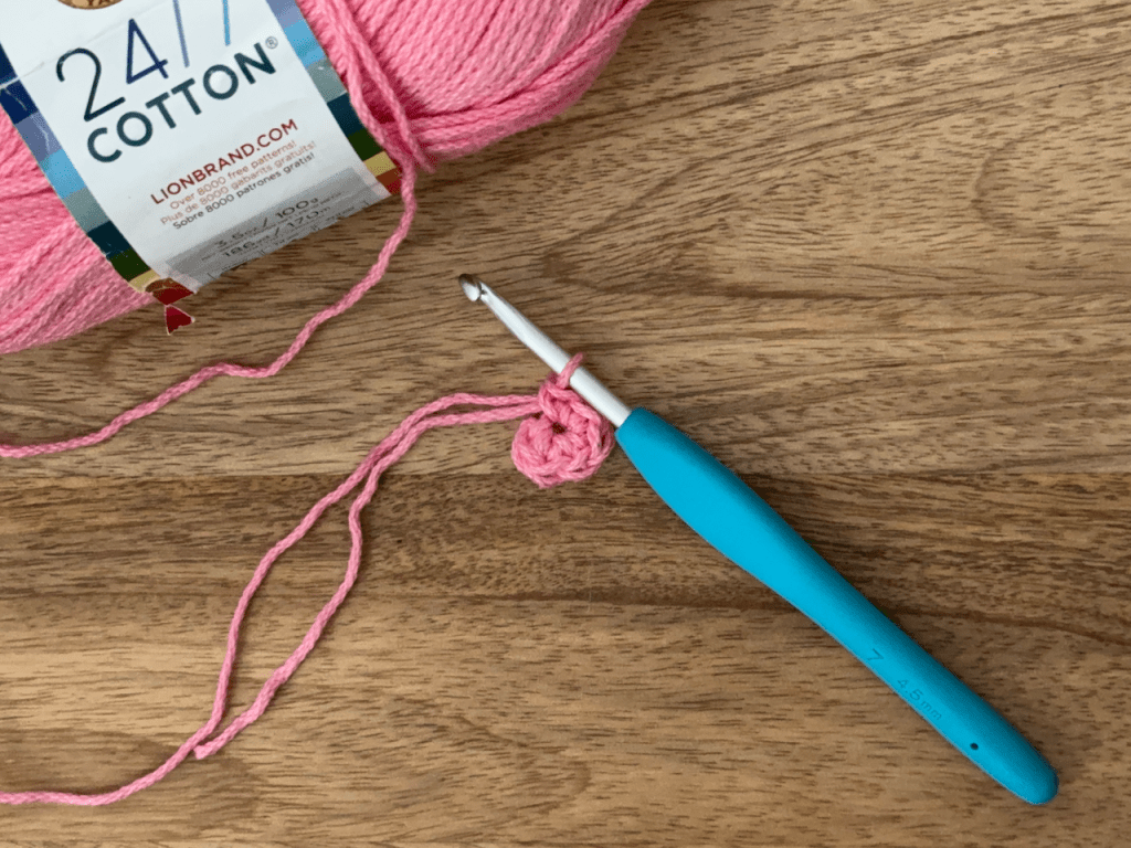 a blue crochet hook and pink yarn with 6 crochet stitches in a magic ring